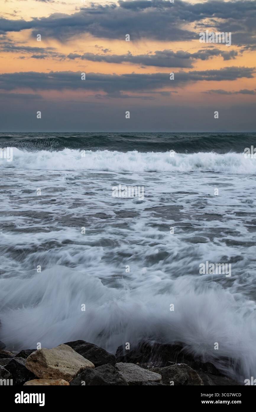 Ozeanwellen, die bei Sonnenuntergang gegen Felsen krachen Stockfoto