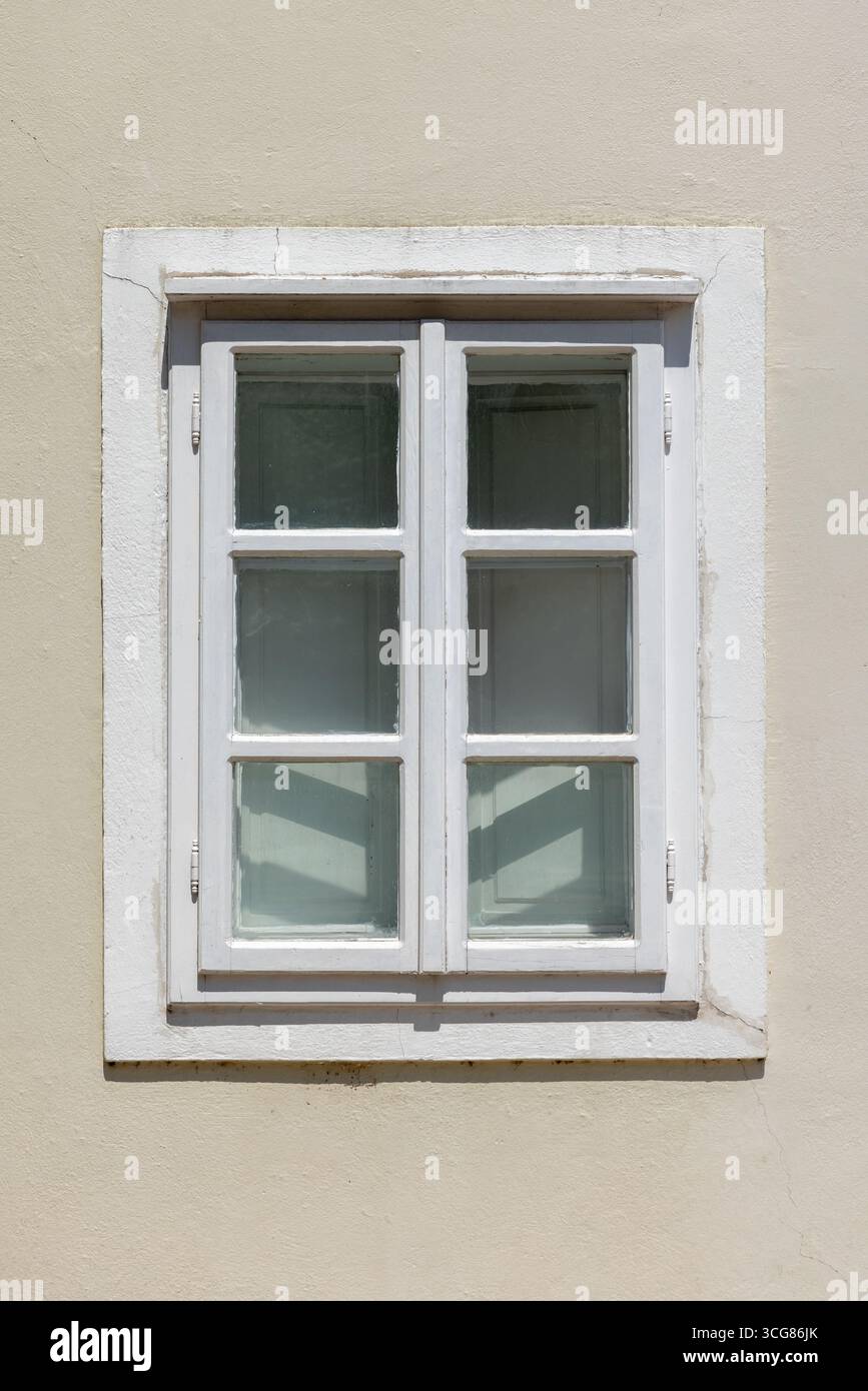 Fenster in weißem Holzrahmen, an einer beigefarbenen Stuckwand mit weichem Tageslicht. Vorderansicht, Hintergrundfotostruktur Stockfoto