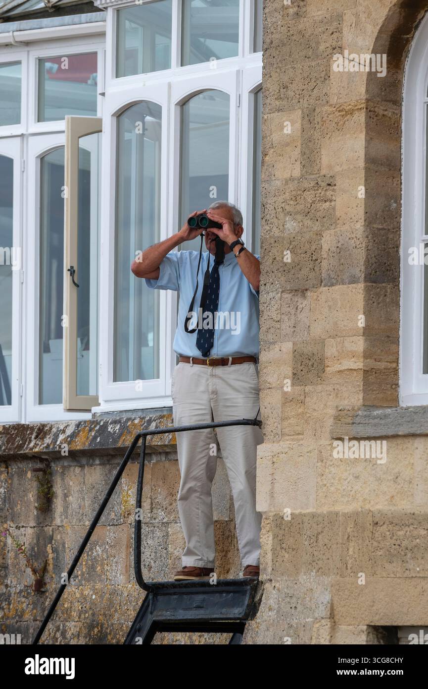Älterer Mann Mitglied der königlichen Yachtstaffel in Cowes, der die Yachtrennen während der Cowes-Woche mit einem Fernglas ansieht, offizielles IOW der Cowes-Woche. Stockfoto