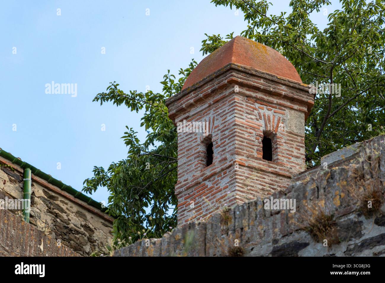 Ein Backsteinwachturm krönt den Burgwall mit seinen kleinen Schlitzfenstern und der Terrakotta-Kuppel, die über die Blätter entlang des befestigten Randes von Collioure hinausragen. Stockfoto