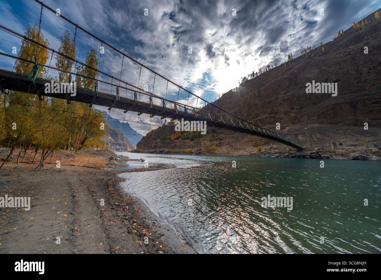Blick auf eine lange Hängebrücke, die sich über einen Fluss unter einem dramatischen Himmel erstreckt und mit einem steilen Hügel verbunden ist, Yasin Valley, Gilgit Baltistan, Pakis Stockfoto