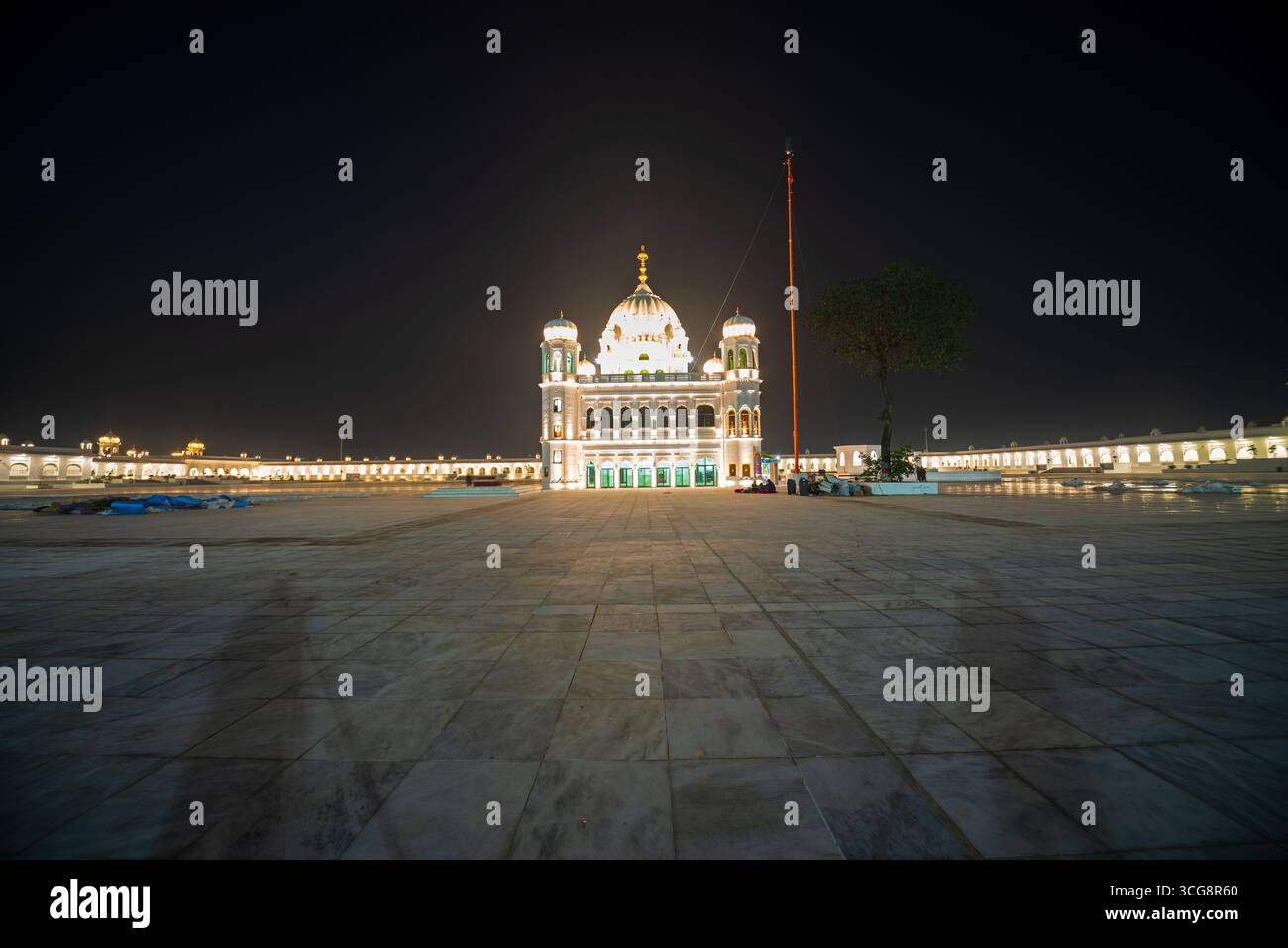 Blick auf den beleuchteten Kartarpur Korridor schimmert vor dem dunklen Himmel, seine weiße Fassade und die goldene Kuppel ein Leuchtturm der Ruhe und Gelassenheit, Kartarpur, Punjab, Pakistan. Stockfoto