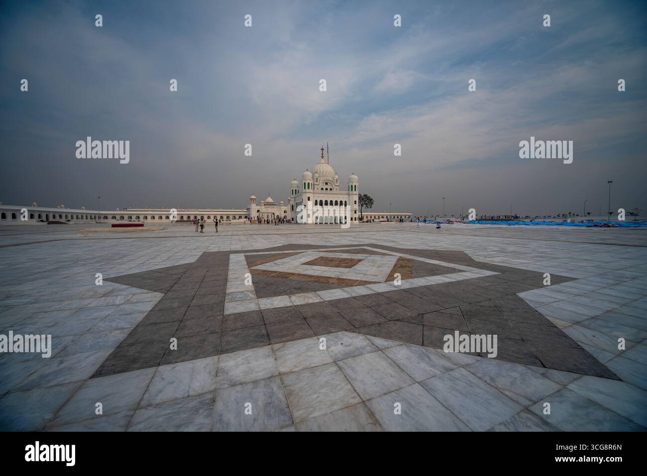 Blick auf die unberührte weiße Gurdwara Kartarpur Sahib, die unter einem gedämpften Himmel schimmert, eingerahmt von einem aufwändig gemusterten Marmorvordergrund, Kartarpur, Punjab, Pakistan. Stockfoto