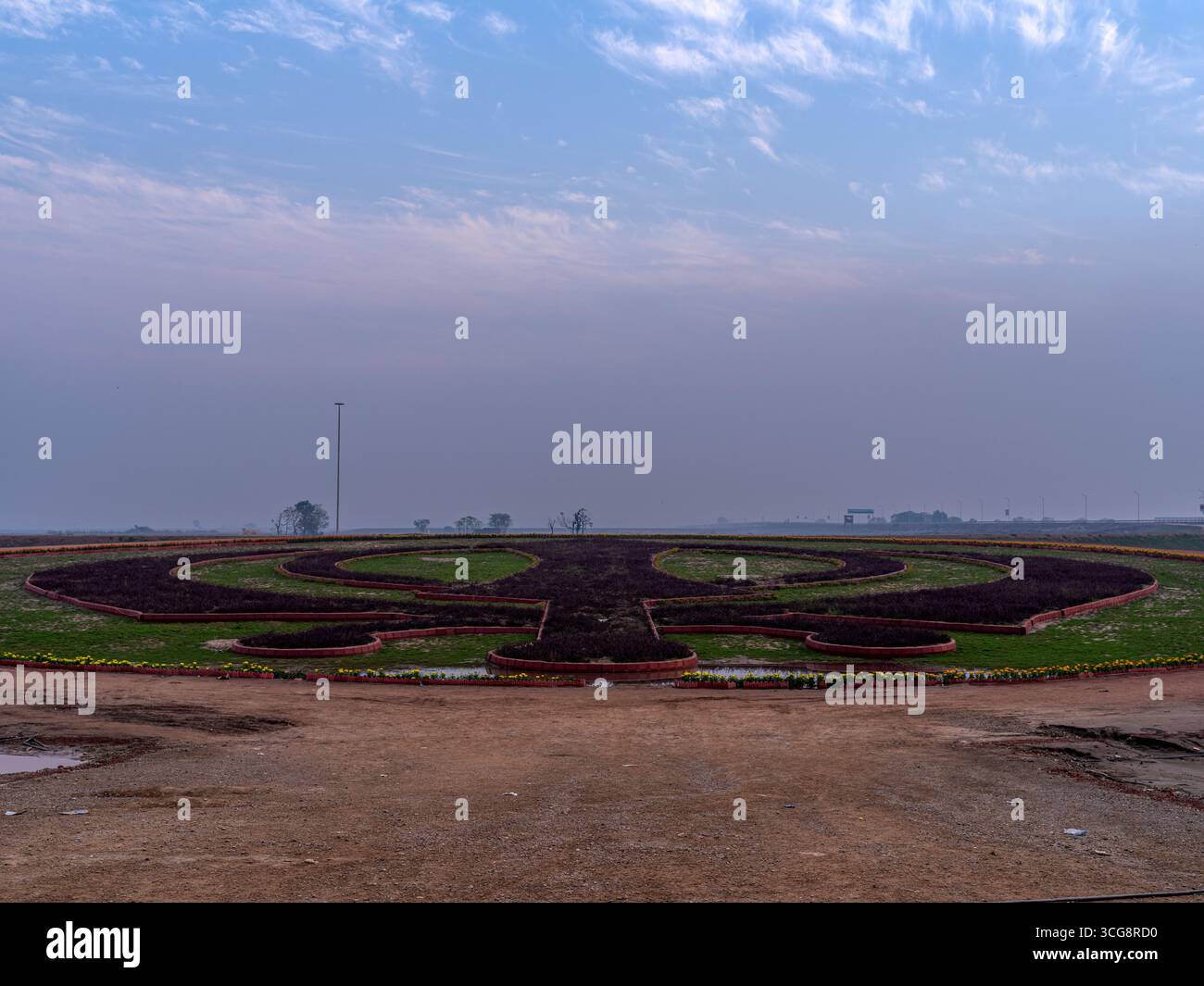 Blick auf ein weitläufiges Wahrzeichen des Sikhismus, ein Khanda aus dunklem Laub und lebendigem grünem Gras, unter einem hellen Himmel, Kartarpur, Punjab, Pakistan. Stockfoto