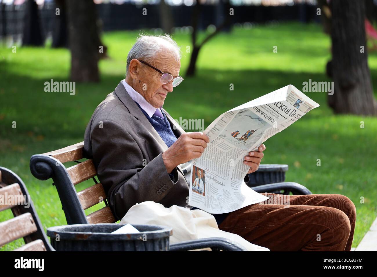 Moskau, Russland - 26. August 2025: Ein alter Mann liest russische Zeitung auf der Straßenbank der Stadt Stockfoto