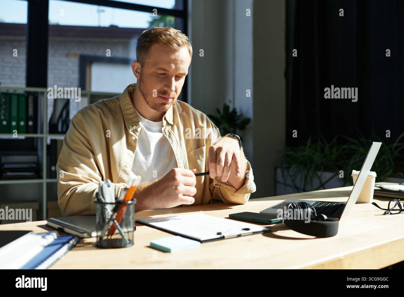 Junge Profis konzentrieren sich auf Aufgaben an einem schlanken Schreibtisch voller Dokumente und Gadgets. Stockfoto