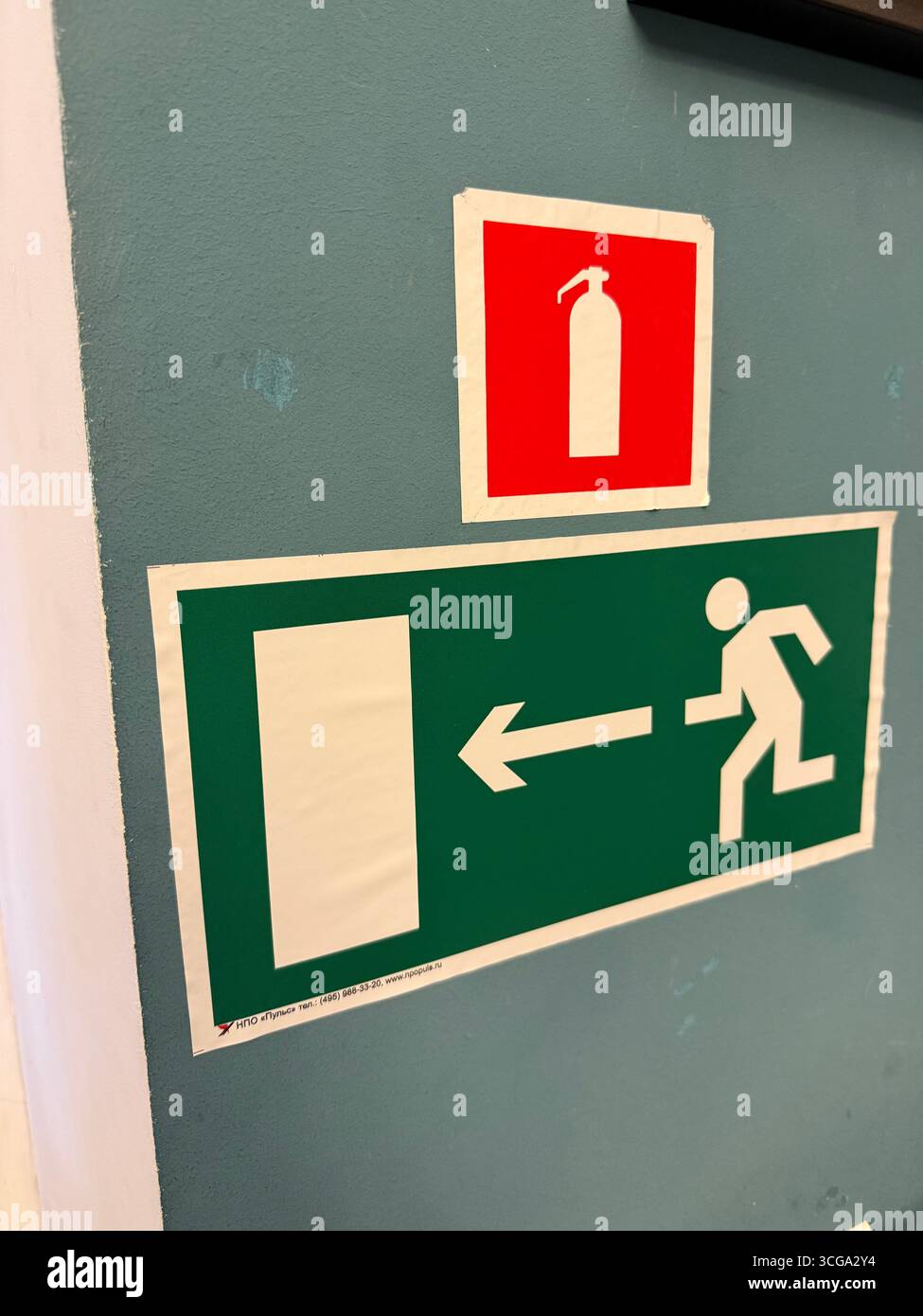 Feuerlöscher und Notausstiegsschilder an einer blauen Wand als Hintergrund für Sicherheitsanweisungen. Mobiles Foto Stockfoto