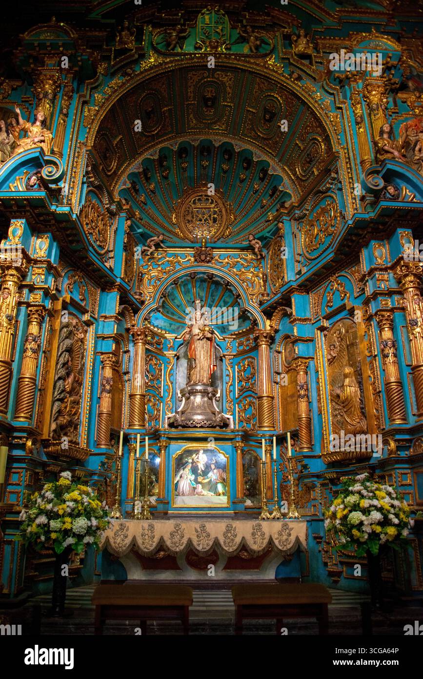 Innenraum der Kathedrale mit gewölbten Decken, goldenen Rippen, verzierten Altar, Holzbänken, Kronleuchtern, karierter Boden und symmetrische Architektur Stockfoto