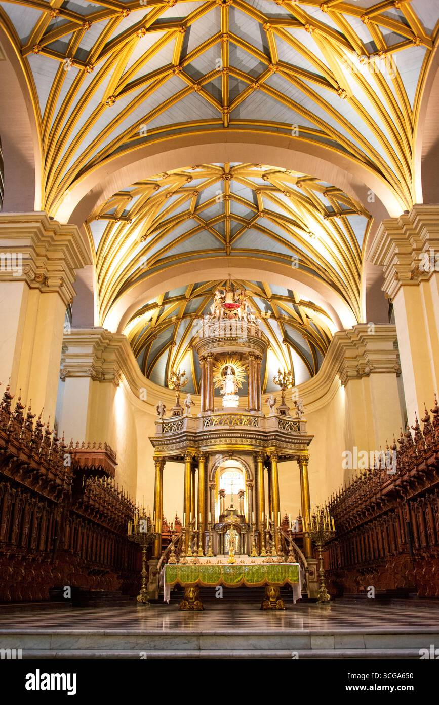 Innenraum der Kathedrale mit gewölbten Decken, goldenen Rippen, verzierten Altar, Holzbänken, Kronleuchtern, karierter Boden und symmetrische Architektur Stockfoto