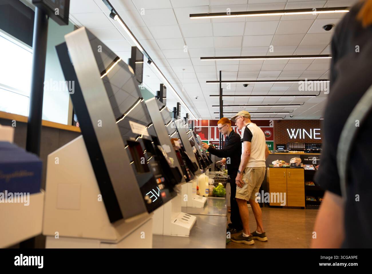 M&S-Mitarbeiter Mitarbeiter Mitarbeiter junger Mann, der älteren älteren älteren Kunden hilft Marks & Spencer Store Self-Service-Bildschirme zur Kasse UK KATHY DEWITT Stockfoto