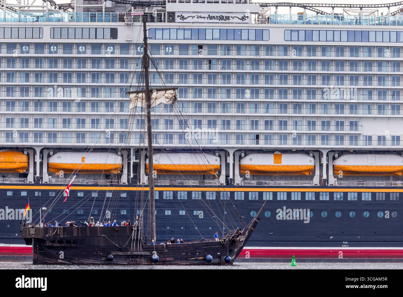 Wismar, Deutschland. August 2025. Die „Wisemara“, eine Nachbildung eines alten Zahnrads vor der Insel Poel, passiert das neue Kreuzfahrtschiff „Disney Adventure“ am ausgerüsteten Kai der Werft von Wismar. Nach rund sieben Jahren Bauzeit wird eines der größten Kreuzfahrtschiffe der Welt in den nächsten Tagen die Hansestadt verlassen. Die US-Reederei Disney Cruise Line übernahm das Schiff vom Insolvenzgut und lässt es von der Meyer Werft in Papenburg, Niedersachsen, bauen. Das Schiff wird für die Disney Group in Südostasien eingesetzt werden Stockfoto