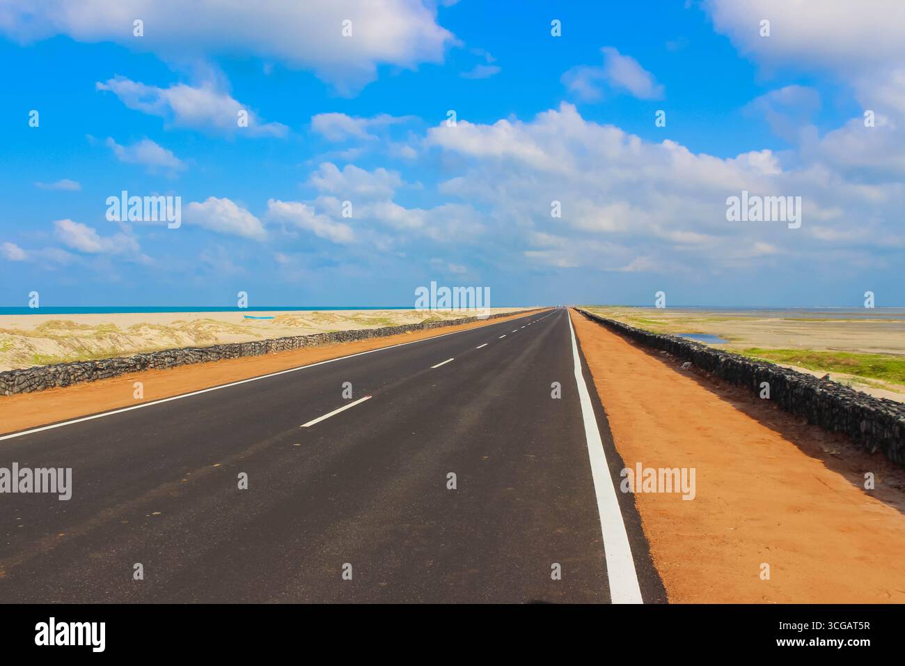 Auf dem Weg nach Dhanuschkodi führt eine enge Straße, die vom Meer flankiert wird, zu den eindringlichen Ruinen der Geisterstadt, die einen atemberaubenden Blick auf das Meer und die Geschichte bietet. Stockfoto