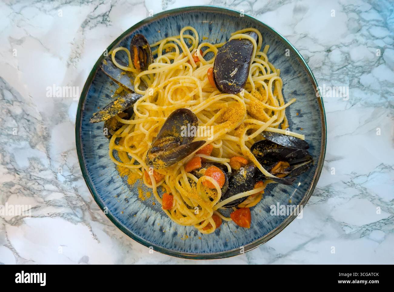 Köstliche Linguine mit Meeresfrüchten, Muscheln, Kirschtomaten und Bottarga, serviert auf blauem Keramikteller Stockfoto