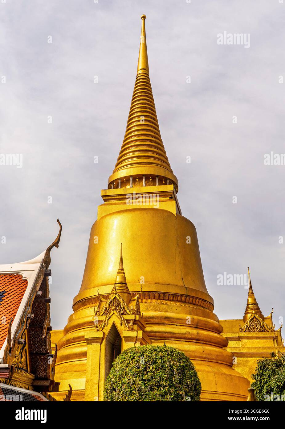 Ein Blick aus der Nähe auf eine goldene Stupa mit einem spitzen Turm, umgeben von üppigem Grün und traditioneller Architektur Stockfoto