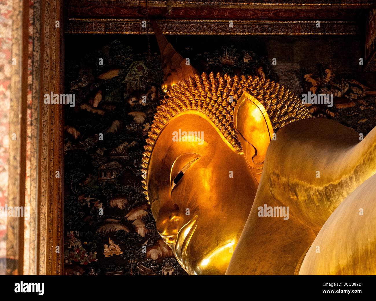 Aus nächster Nähe sehen Sie eine goldene liegende buddha-Statue, die komplizierte Details und Texturen vor einem dunklen Hintergrund mit verzierten Wanddekorationen zeigt Stockfoto