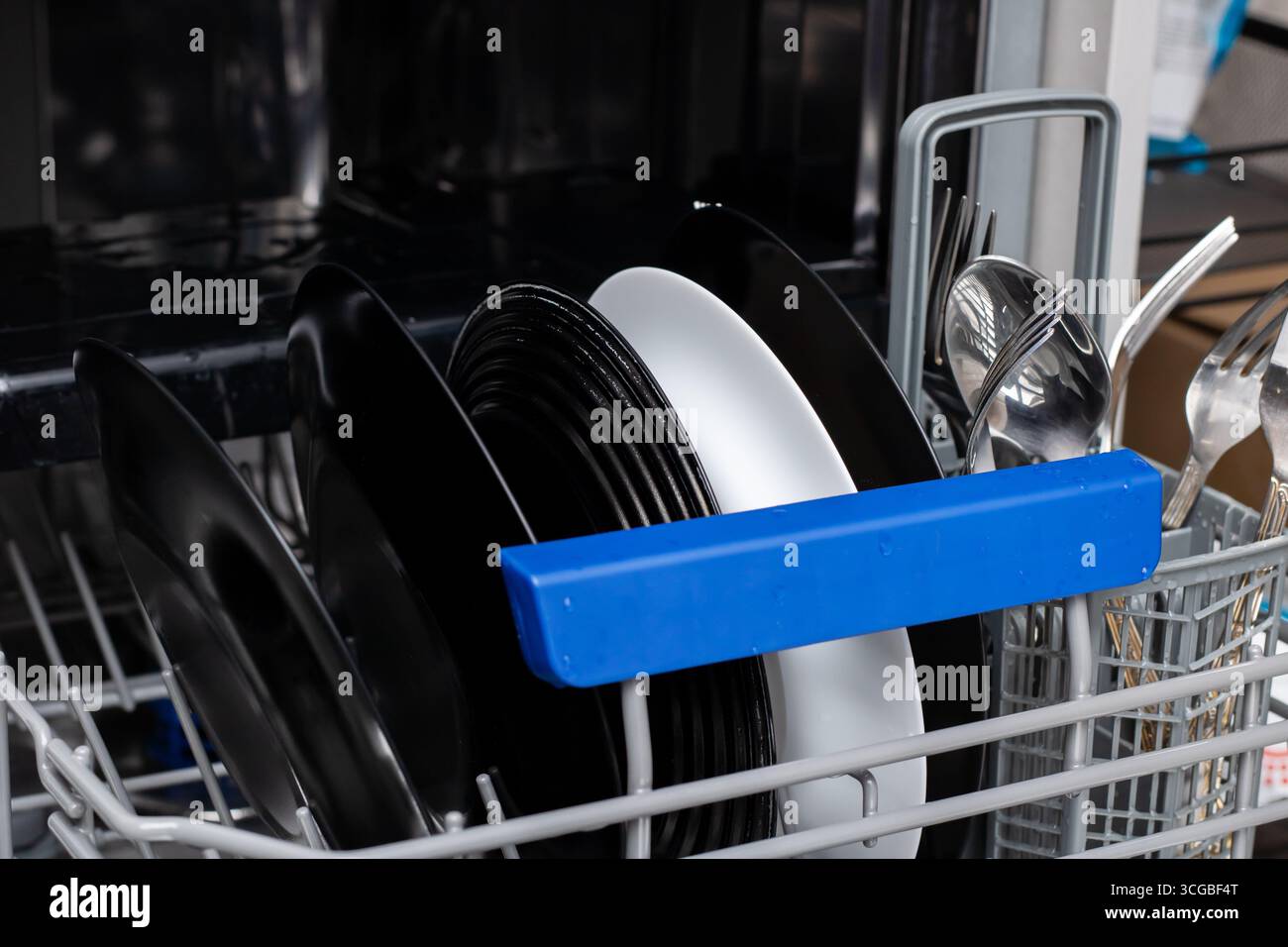 Ein Geschirrspüler mit ordentlich angeordneten schwarz-weißen Tellern und Besteck, die eine effiziente Organisation für eine saubere Küche darstellen. Stockfoto