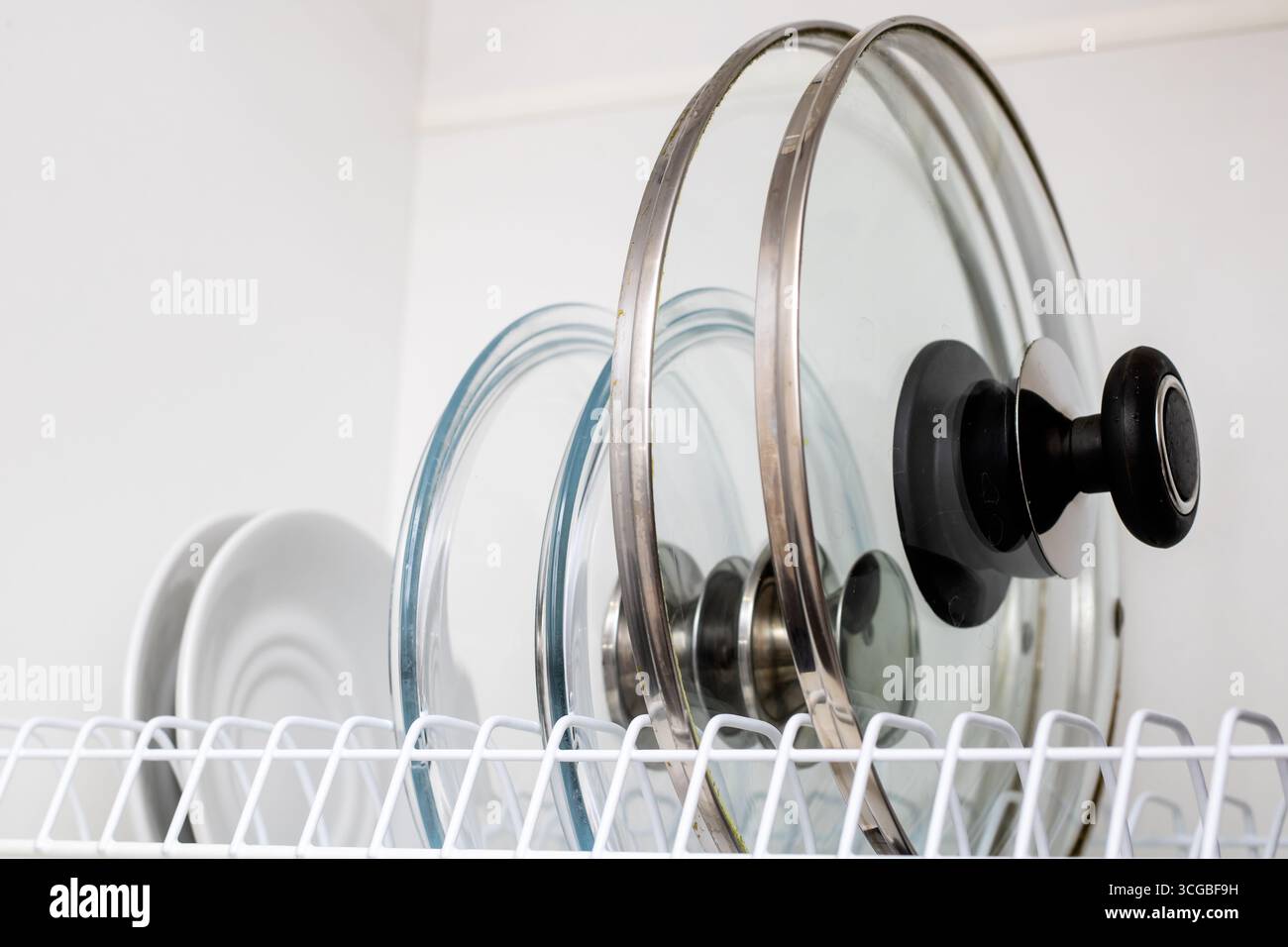 Eine ordentlich angeordnete Sammlung von Glaskochtopf-Deckeln in einem Lagerregal, die die Organisation der Küche verbessern und den Zugang für Küchenchefs verbessern. Stockfoto