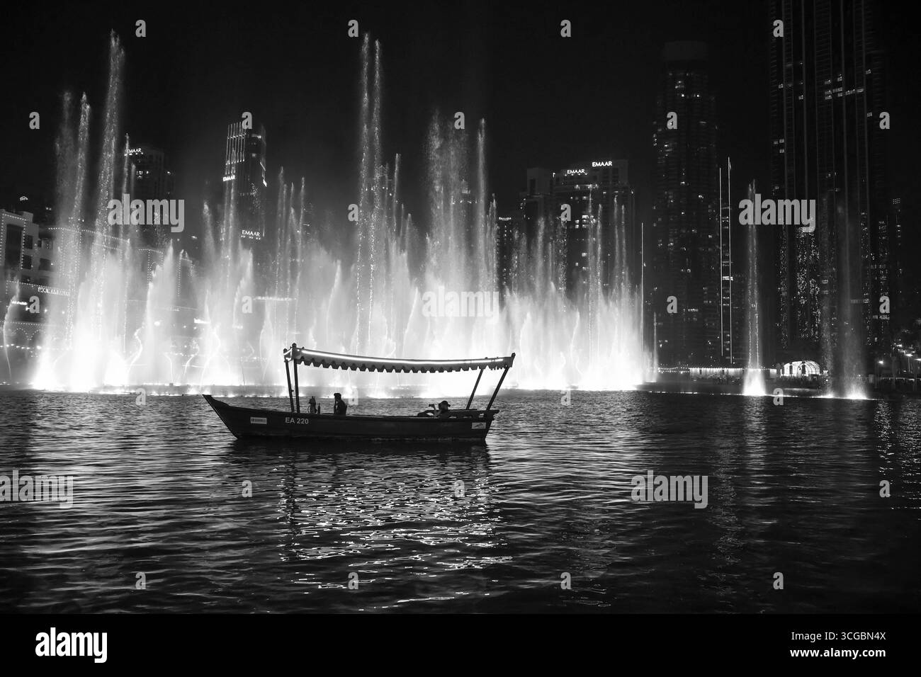 Glitzernde Skyline von Dubai bei Nacht mit beleuchteten Wolkenkratzern, Türmen, Wasser, Booten und pulsierendem Stadtleben im Nahen Osten. Stockfoto