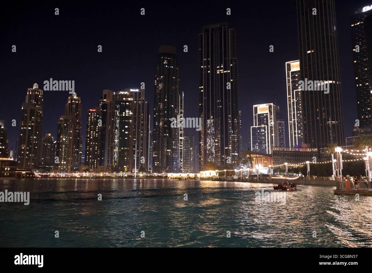 Glitzernde Skyline von Dubai bei Nacht mit beleuchteten Wolkenkratzern, Türmen, Wasser, Booten und pulsierendem Stadtleben im Nahen Osten. Stockfoto
