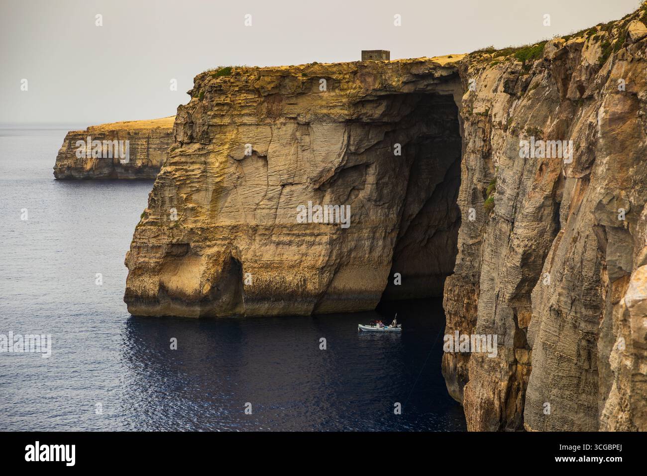 Gozo, Malta – 23. Juni 2021: Kleines Boot mit Menschen in der Nähe von hoch aufragenden Kalksteinklippen entlang der Mittelmeerküste. Stockfoto