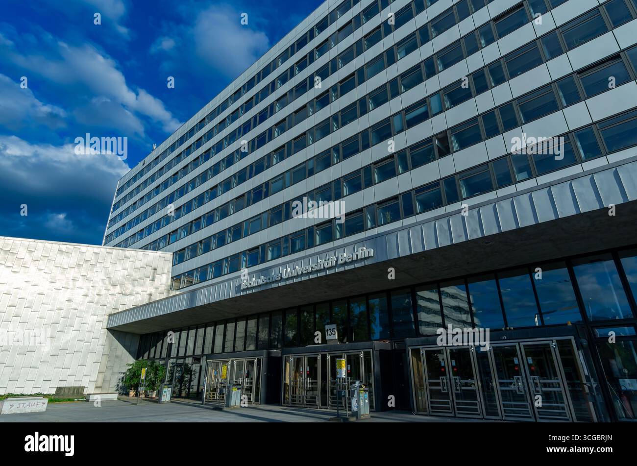 Vorderansicht des Hauptgebäudes der TU Berlin mit Glastüren und dynamischen Sommerwolken über Charlottenburg. Stockfoto
