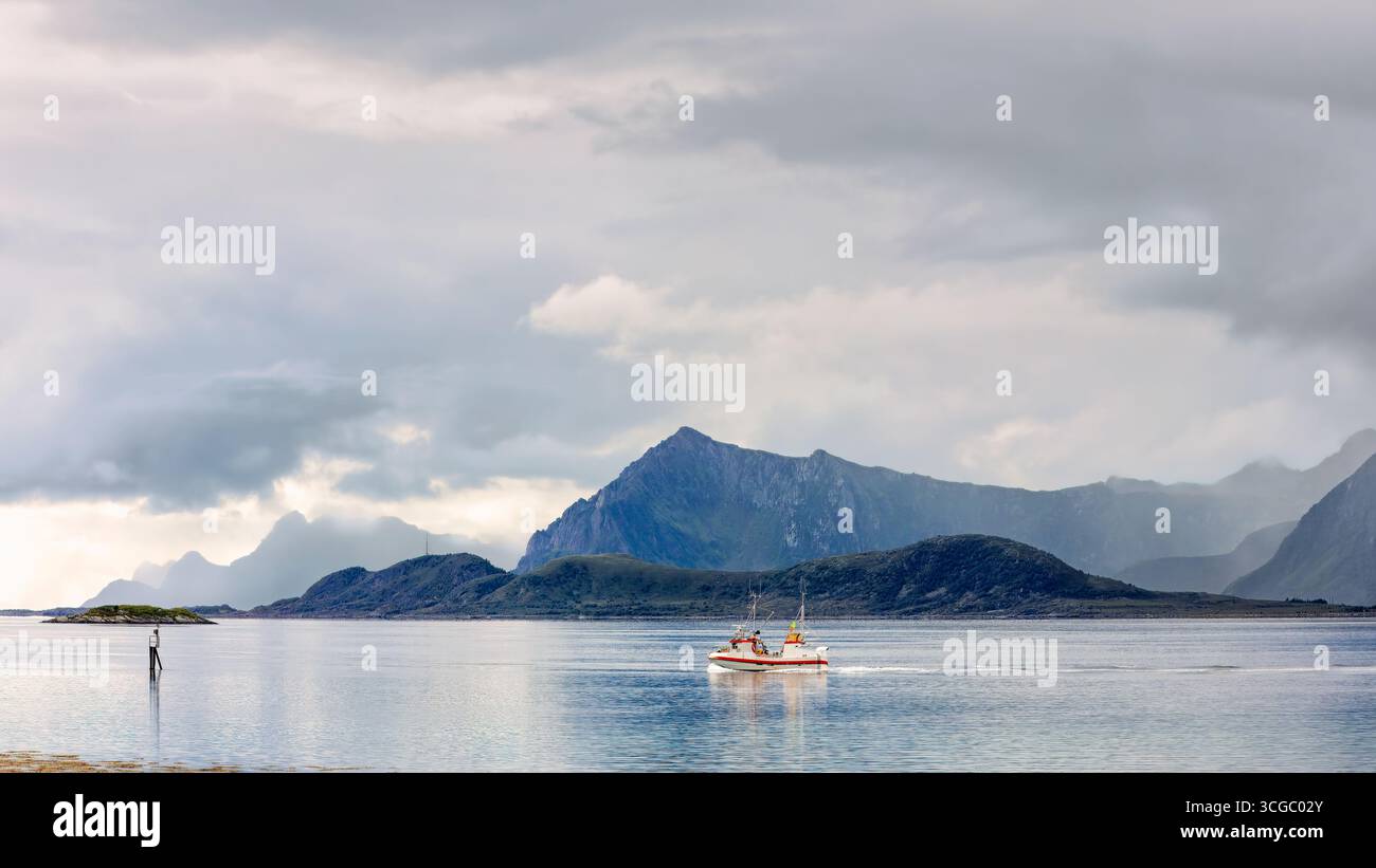 Fischerboot gleitet durch ruhige Gewässer mit Bergen im Hintergrund und schafft eine friedliche und malerische Landschaft. Lofoten-Inseln, Gimsoy, N Stockfoto