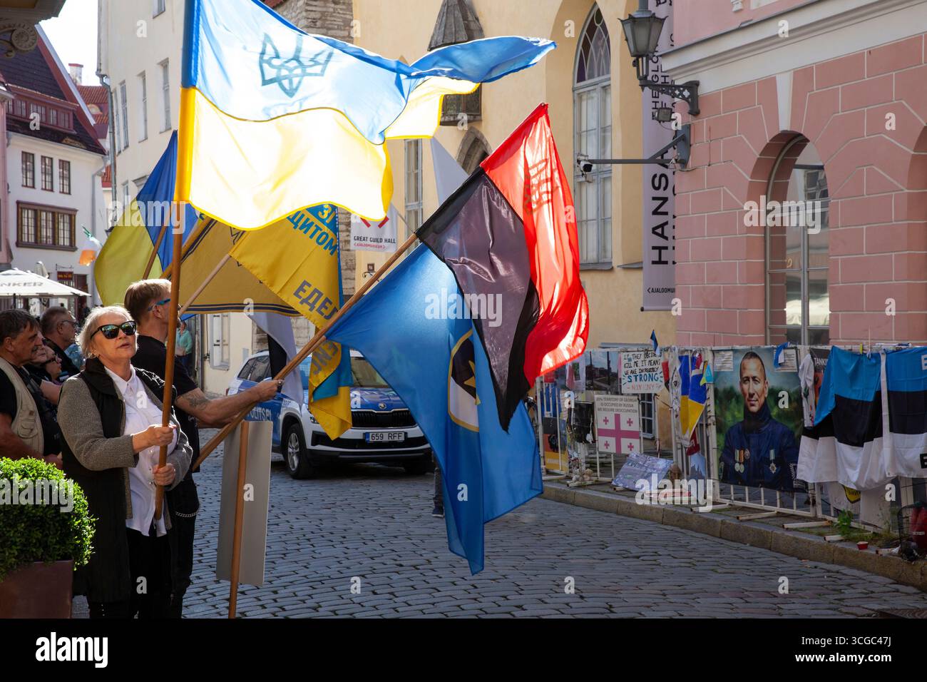 Tallinn, Estland, 27. August 2025: Vor der russischen Botschaft in Estlands Hauptstadt findet wöchentlich ein Protest gegen die Regierungspolitik statt. Die Demonstranten kritisierten Russlands Invasion in der Ukraine und Georgien und seine internen Durchgreifungen der Redefreiheit. Sie riefen auf Russisch Slogans, die den Botschaftsmitarbeitern direkt gegenüber einer engen Kopfsteinpflasterstraße in der Stadt des UNESCO-Weltkulturerbes deutlich zu hören gewesen sein müssen. Die rote und schwarze Version der ukrainischen Flagge repräsentiert die ukrainische Aufständische Armee (UPA). Schutzbarrieren außerhalb der Botschaft sind in Plakaten und Protesterklärungen verdeckt Stockfoto
