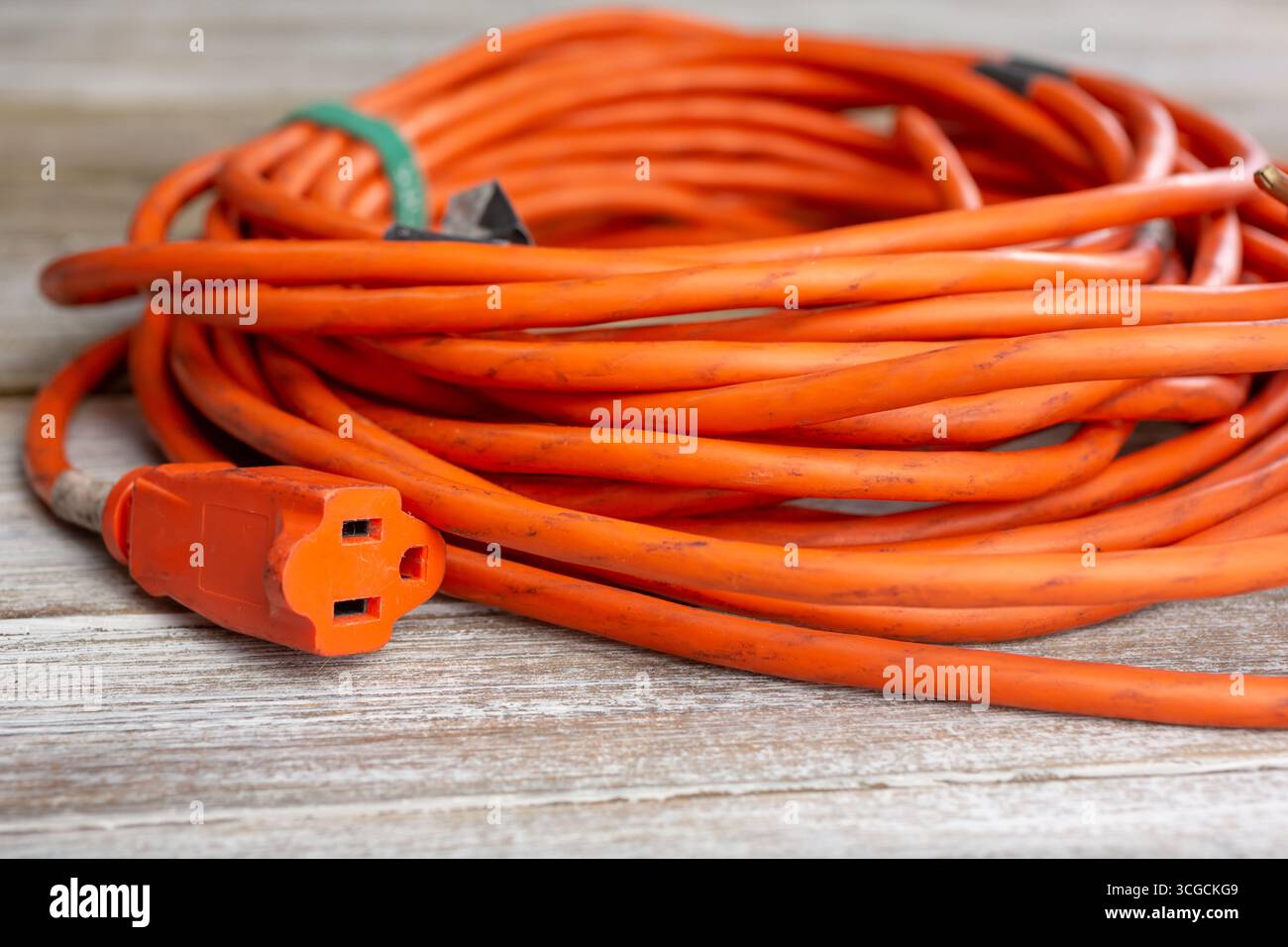 Ansicht eines orangefarbenen Verlängerungskabels mit Steckerbuchse auf einer Holzoberfläche. Stockfoto