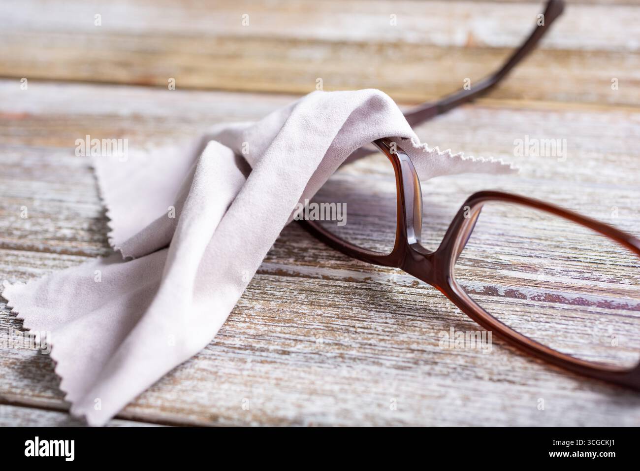 Eine Nahaufnahme einer Brille mit einem Mikrofaser-Reinigungstuch auf einer Holzoberfläche. Stockfoto