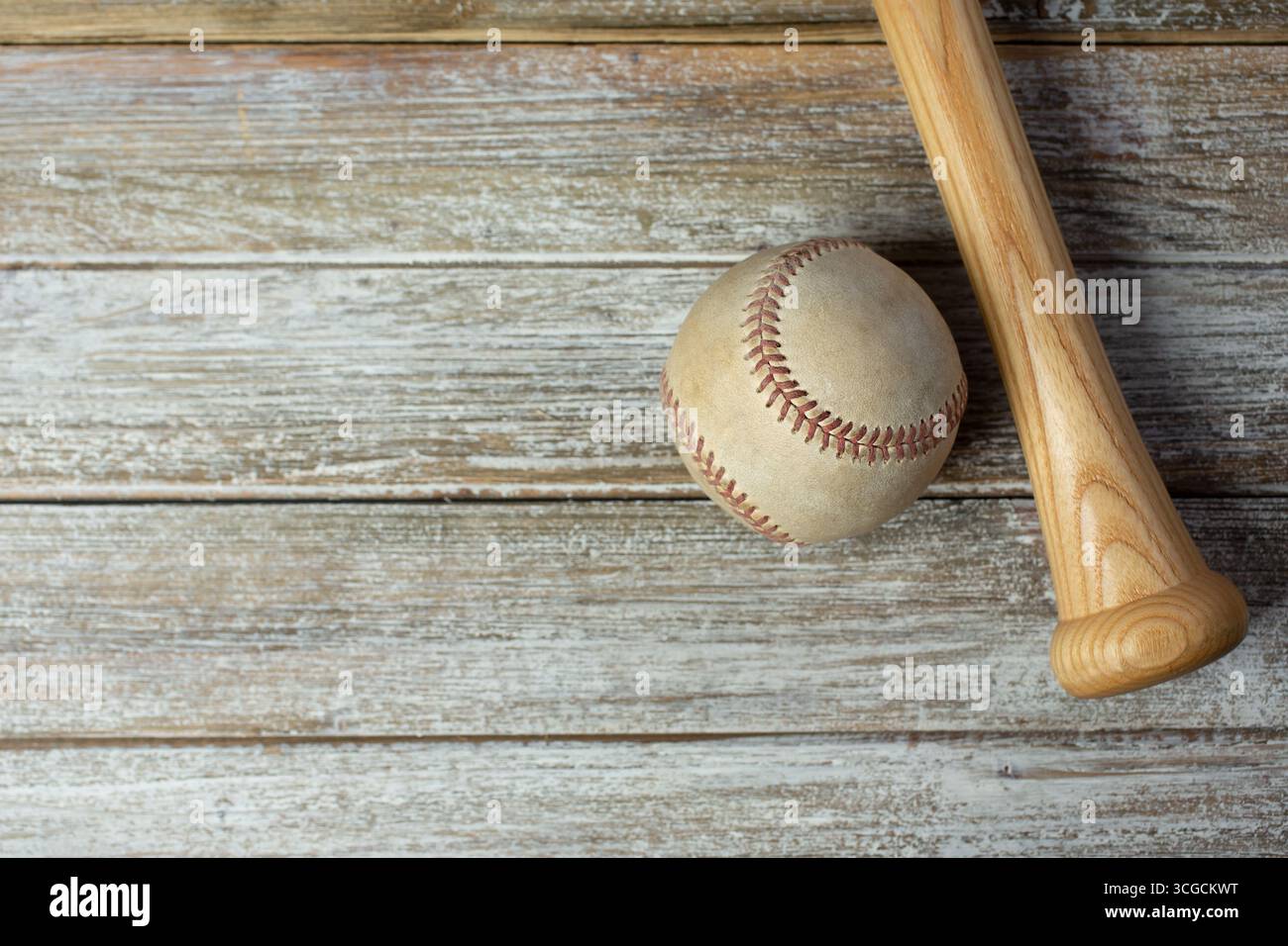 Eine Ansicht von oben nach unten auf einen abgenutzten Baseball und den unteren Griffbereich eines hölzernen Baseballschlägers auf einer hölzernen Oberfläche als Hintergrundbild. Stockfoto