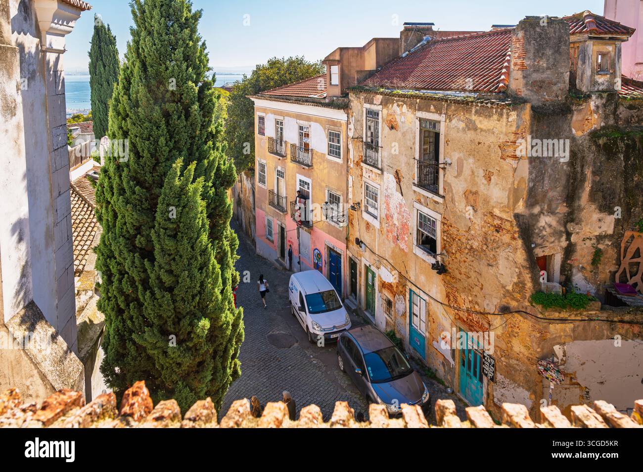 Ein Musiker steht auf einem Balkon und singt Passanten auf der Kopfsteinpflasterstraße unten im hügeligen mittelalterlichen Alfama-Viertel in Lissabon, Portugal. Stockfoto