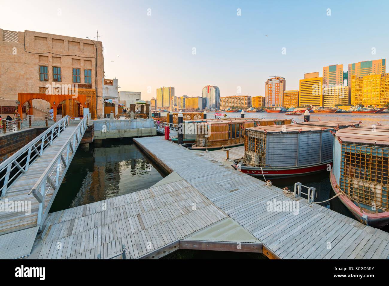 Traditionelle Fährboote und Abras legen bei Sonnenuntergang entlang der Al Seef Shopping, Restaurants und Uferpromenade in der Innenstadt von Dubai, Vereinigte Arabische Emirate, an Stockfoto