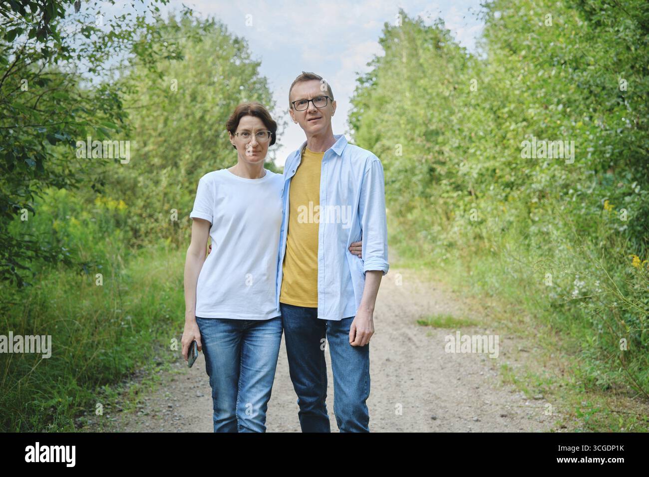 Ein Paar mittleren Alters steht auf einem natürlichen Pfad, umgeben von üppigem Grün, eng zusammen. Sie sind lässig gekleidet und genießen einen entspannten Tag im Freien Stockfoto