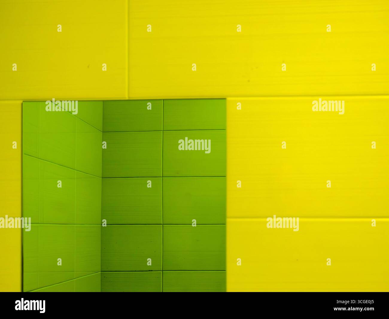 Grüner rechteckiger Spiegel reflektiert grüne Fliesen auf einer gelb gekachelten Wand und schafft ein farbenfrohes und abstraktes geometrisches Design, perfekt für die Innenarchitektur Stockfoto