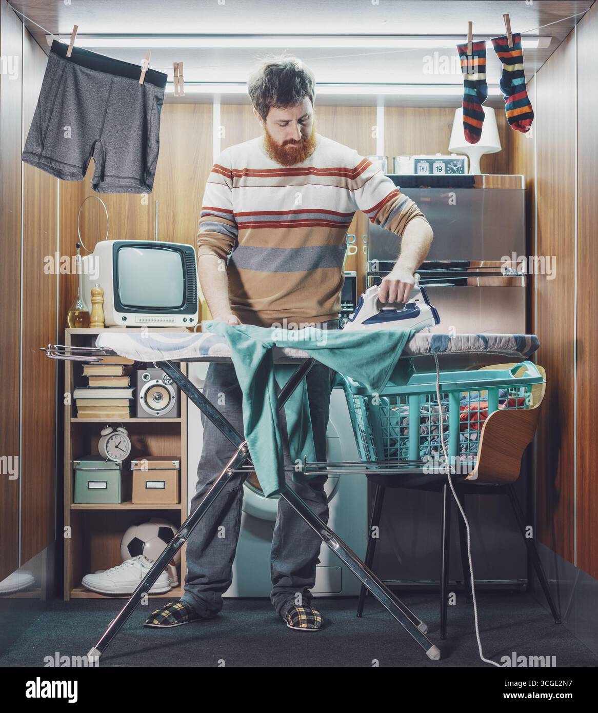 Ein unabhängiger Mann, der allein in einer Mikrowohnung wohnt, bügelt Kleidung Stockfoto