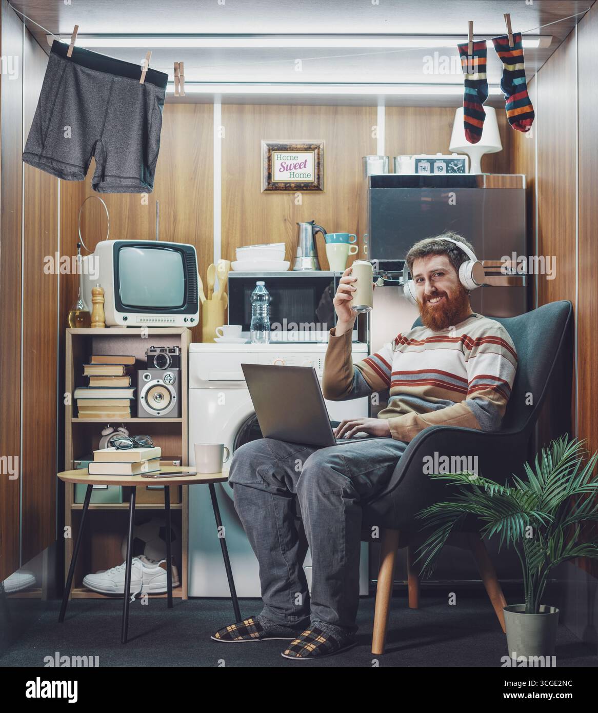 Porträt eines glücklichen, alleinstehenden jungen Mannes, der allein in einer Mikrowohnung lebt: Er trinkt Kaffee und lächelt in die Kamera Stockfoto