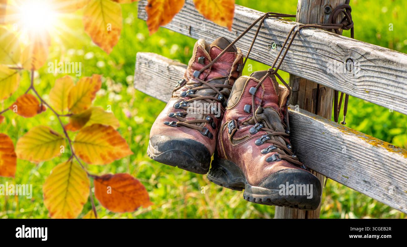 Wandern im Herbst in den Bergen an einem Zaun hängen zwei Wanderstiefel mit Herbstlaub als Symbolbild für Wandern und Erholung im Herbst - FOTOMONTAGE Stockfoto
