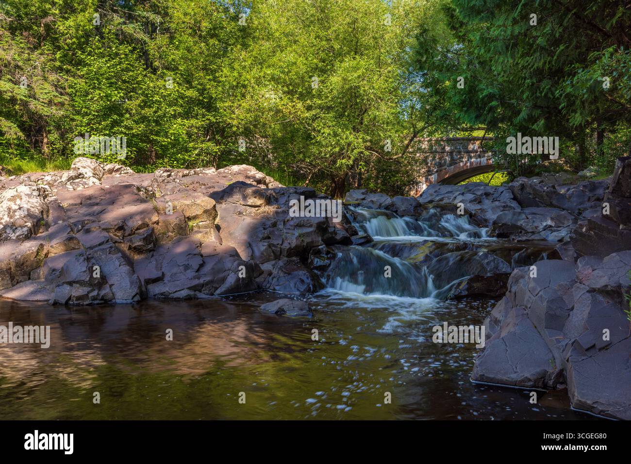 Eine malerische Landschaft mit einer alten Steinbogenbrücke mit einem kleinen Wasserfall auf einem Bach im Wald. Stockfoto