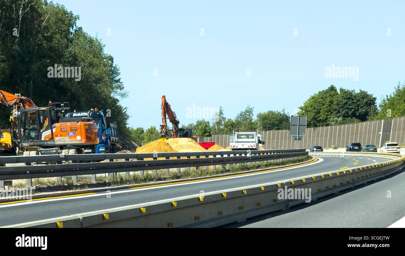 Autobahnbaustelle mit Baggern und Lkw, die in der Nähe von Lärmschutzbarrieren und Waldgebieten arbeiten. Dresden, Deutschland - 19. August 2025 Stockfoto