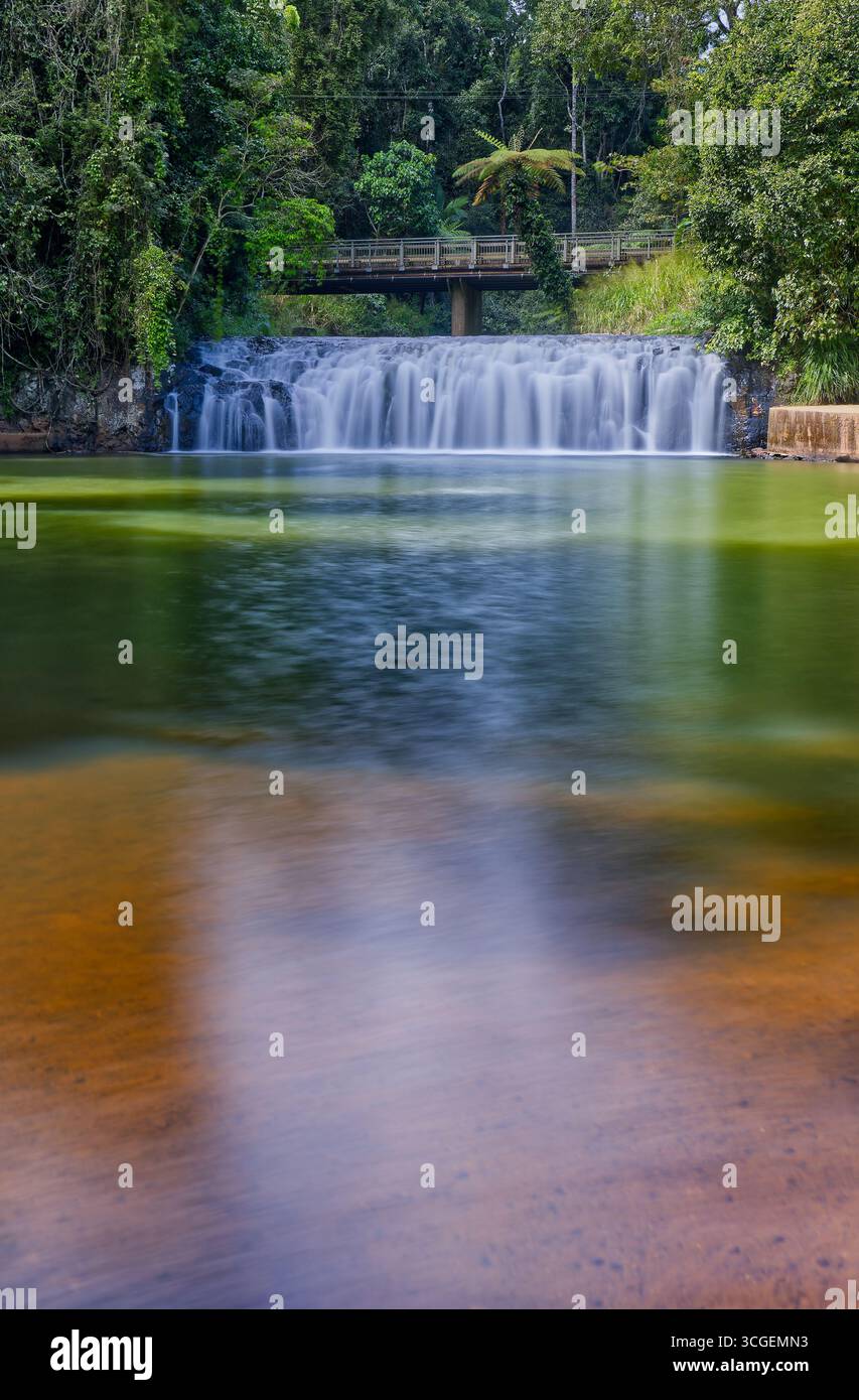 Die Malanda-Wasserfälle kaskadieren auf dem Johnstone River im Regenwald mit einem künstlichen Swimmingpool und einer Brücke in der Morgensonne in Malanda, weit nördlich von Queensland Stockfoto