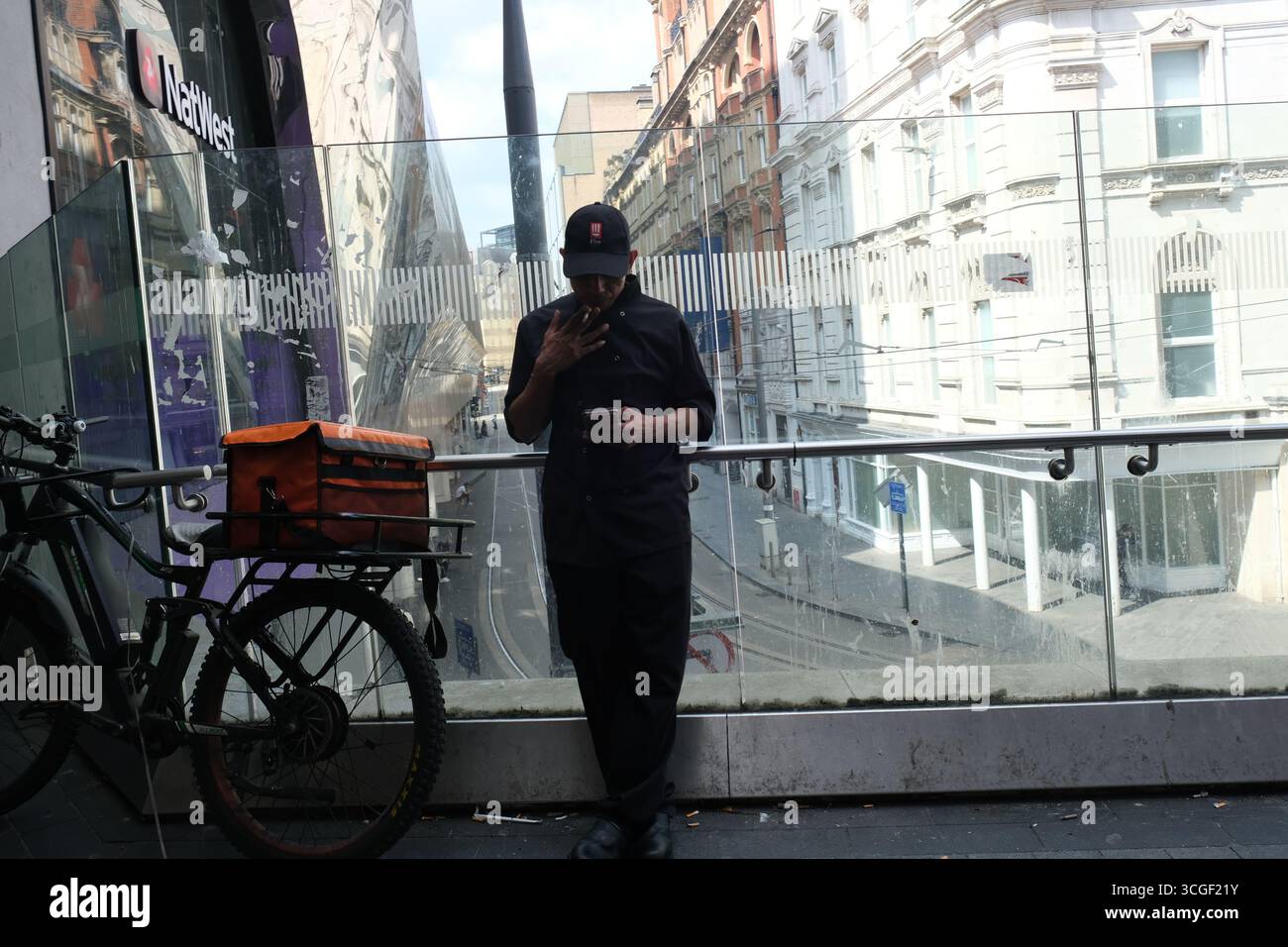 Ein Fahrradfahrer macht eine Zigarettenpause in der Nähe eines Eingangs zur New St Station im Stadtzentrum von Birmingham Stockfoto