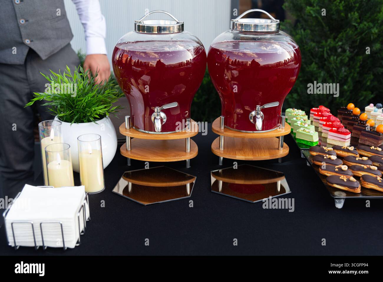 Eine stilvolle Outdoor-Einrichtung mit zwei großen Getränkespendern, gefüllt mit einem leuchtend roten Getränk. Auf dem Tisch finden Sie auch eine Auswahl an bunten Desserts Stockfoto