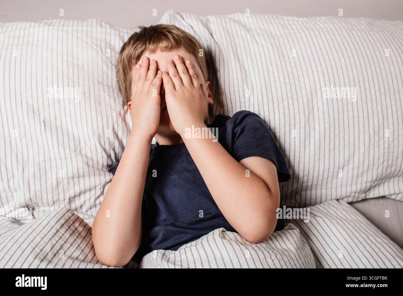 Das Kind hatte Angst vor dem Schlafengehen. Nachtschrecken bei einem Kind. Der Junge bedeckt sein Gesicht mit seinen Händen in Angst. Albträume und Angst vor der Dunkelheit. Stockfoto