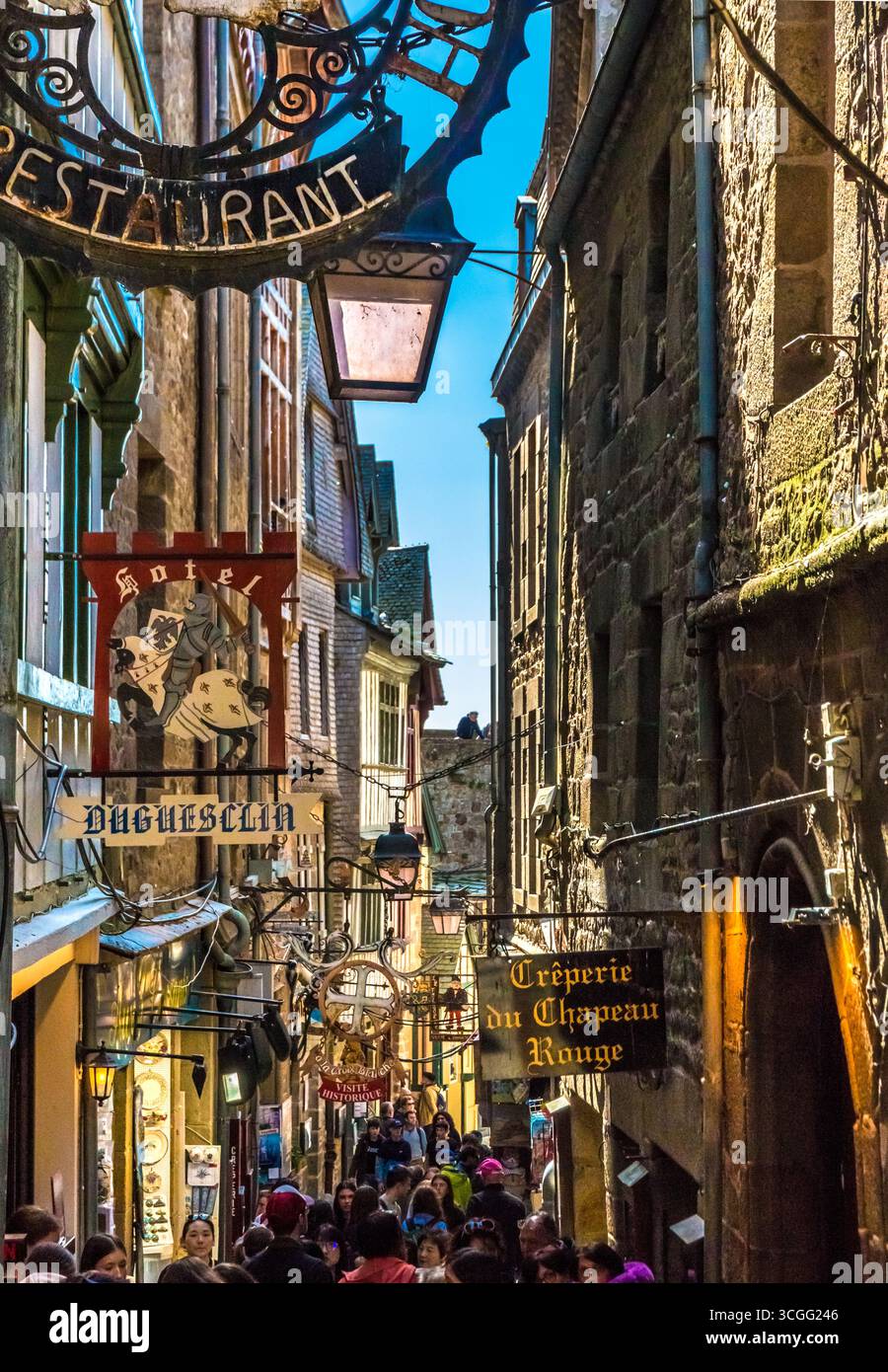 Auffällige Nahaufnahme der Hängeschilder im alten Stil, die sich über der Menge in der Grande Rue des Mont-Saint-Michel bewegen. Viele sind Schmiedeeisen... Stockfoto