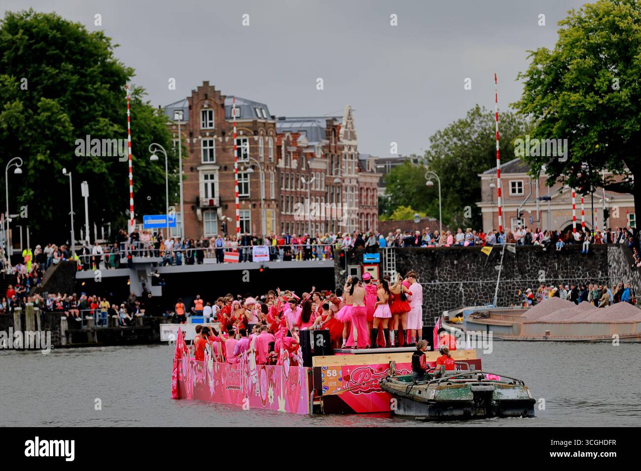 Das pinkfarbene Paradeboot fährt entlang eines Stadtkanals vorbei an Menschenmassen an Böschungen während der Pride Amsterdam Canal Parade in Amsterdam, Niederlande. Stockfoto