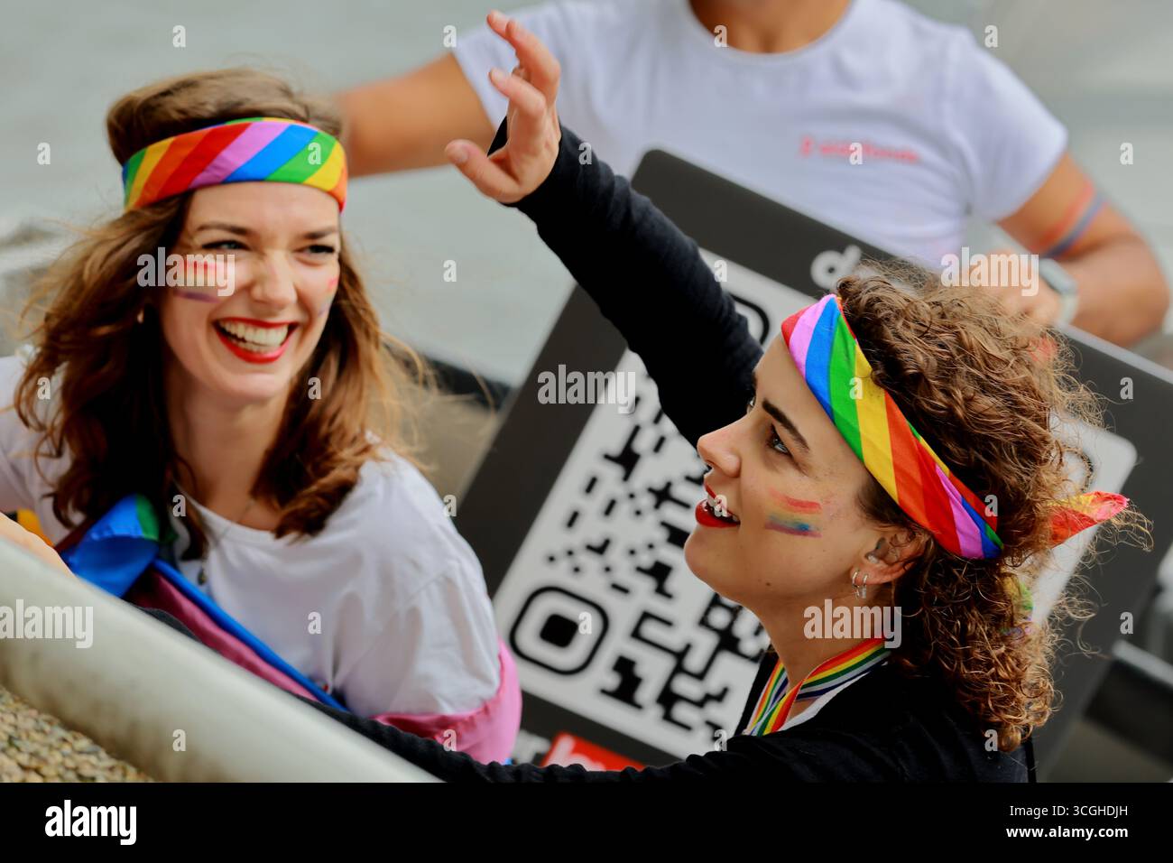 Zwei Teilnehmer mit Regenbogenbügeln lächeln und winken an Bord einer Pride Amsterdam Canal Parade in Amsterdam, Niederlande, während der festlichen Veranstaltung. Stockfoto