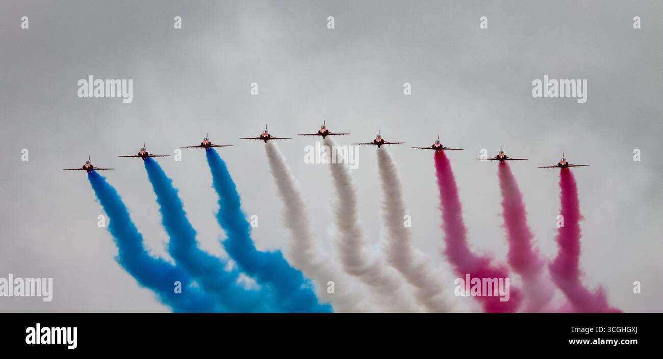Rote Pfeile Kunstflugteam fliegt in Formation und setzt farbige Rauchspuren in Blau, weiß und Rot gegen einen bewölkten Himmel frei RIAT 2025 Stockfoto