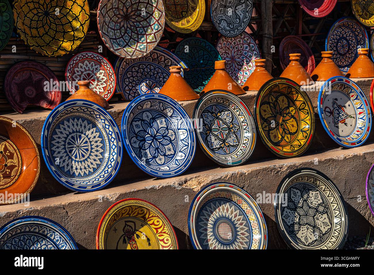 Farbenfrohe marokkanische Keramikplatten mit komplexen geometrischen Mustern neben Terrakotta-Tagine-Töpfen an einem traditionellen Marktstand Stockfoto