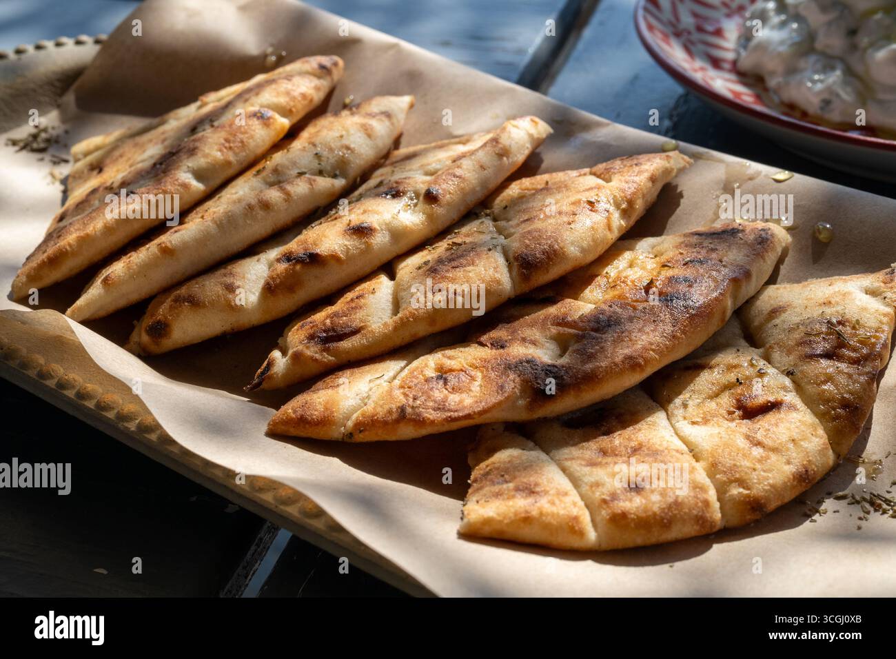 Pita-Brotscheiben mit Honig besprüht, mit Oregano bestreut, auf Holztablett mit Pergamentpapier Stockfoto
