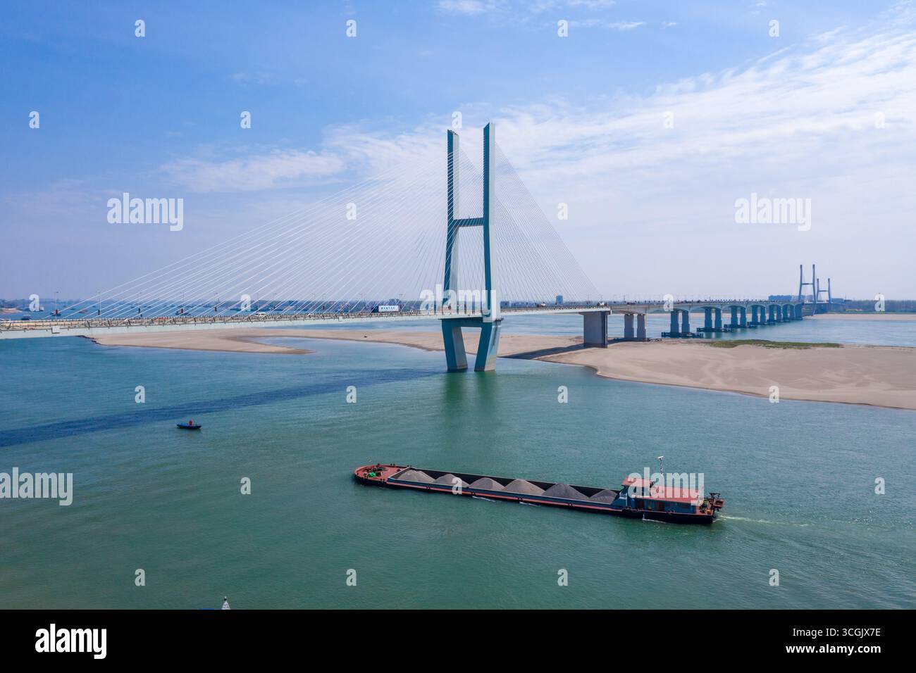 Ein weites Bild zeigt eine große, mit Kabel gehaltene Brücke unter einem hellblauen Himmel. Die Brücke hat zwei hohe Türme und viele Kabel, die zum Straßendeck führen. A BA Stockfoto